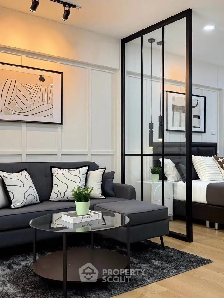 Modern living room with stylish decor and glass partition leading to bedroom, featuring cozy seating and elegant artwork.
