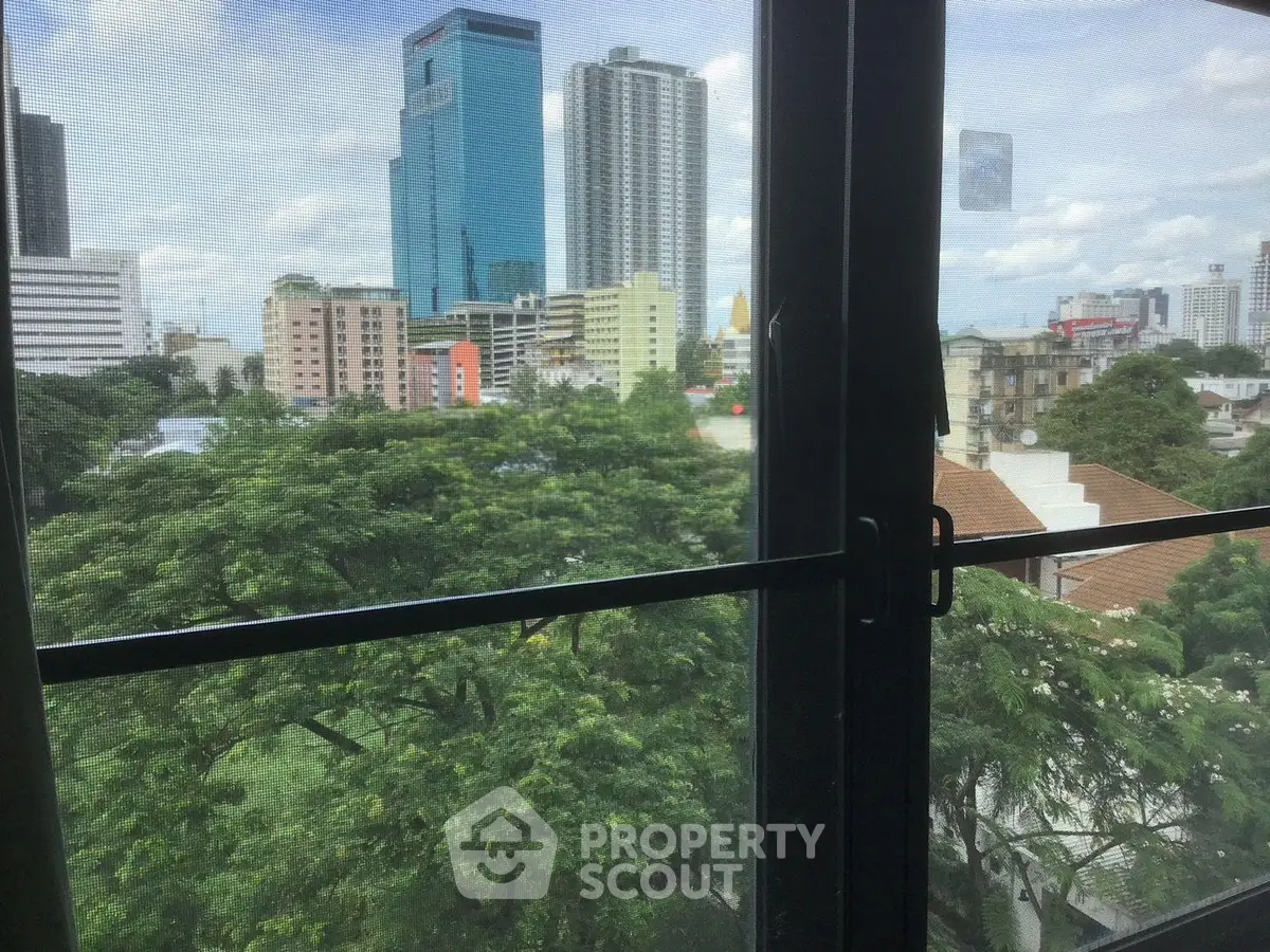Stunning cityscape view from a high-rise window overlooking lush greenery and modern skyscrapers.