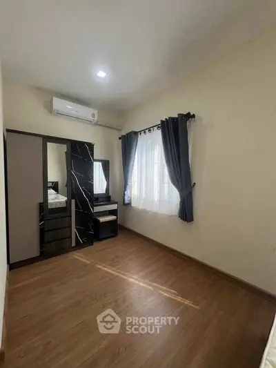 Spacious bedroom with wooden flooring and modern furniture, featuring a large window with curtains.