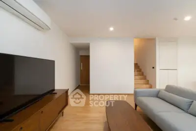 Modern living room with sleek furniture and wooden flooring, featuring a flat-screen TV and minimalist design.