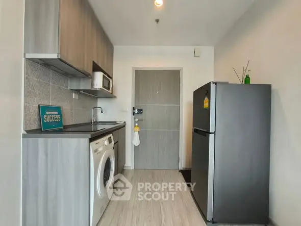 Modern kitchen with washing machine, fridge, and sleek cabinetry in compact layout.