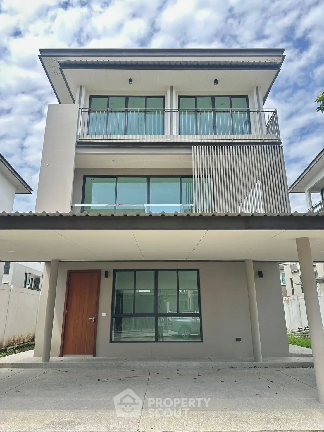 Modern three-story house with sleek design and large windows under a cloudy sky.