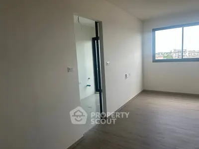 Spacious unfurnished room with large window and wooden flooring, ideal for customization.