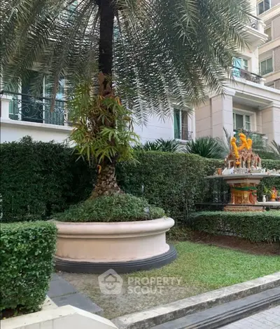 Elegant garden view with lush greenery and a decorative statue in a luxury residential complex.