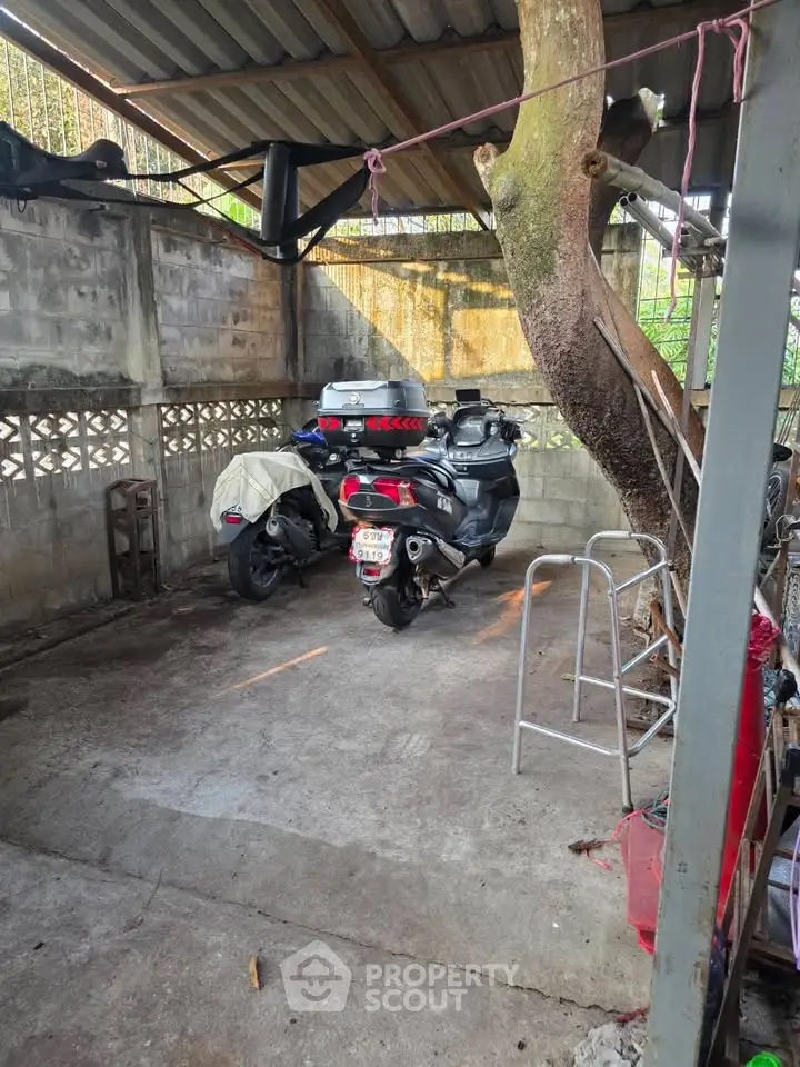 Covered parking area with two motorcycles and a tree, featuring a rustic concrete wall.
