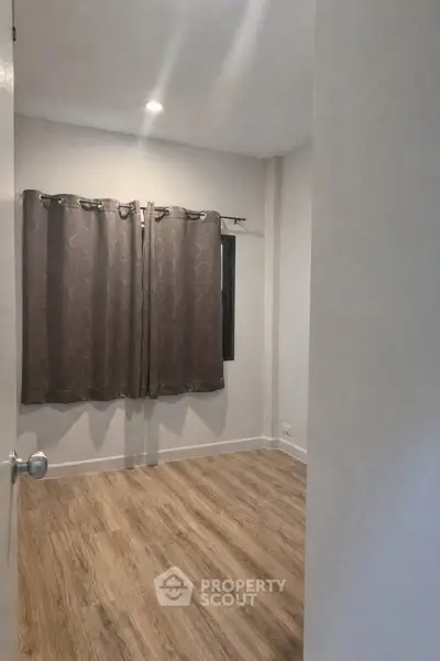 Spacious empty room with wooden flooring and large window, perfect for customization.