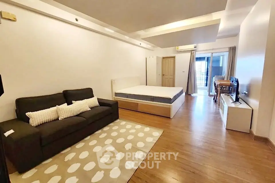 Spacious studio apartment with modern furnishings and wooden flooring, featuring a cozy living area and ample natural light.