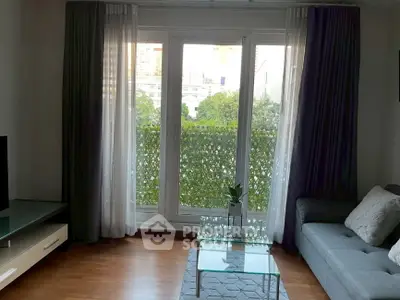 Charming living room with glass coffee table and lush garden view through large windows.