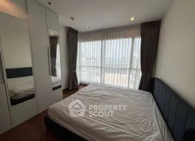 Spacious bedroom with large windows and modern furnishings in a high-rise apartment.