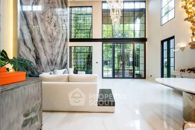 Luxurious living room with high ceilings, marble wall, and garden view through large windows.