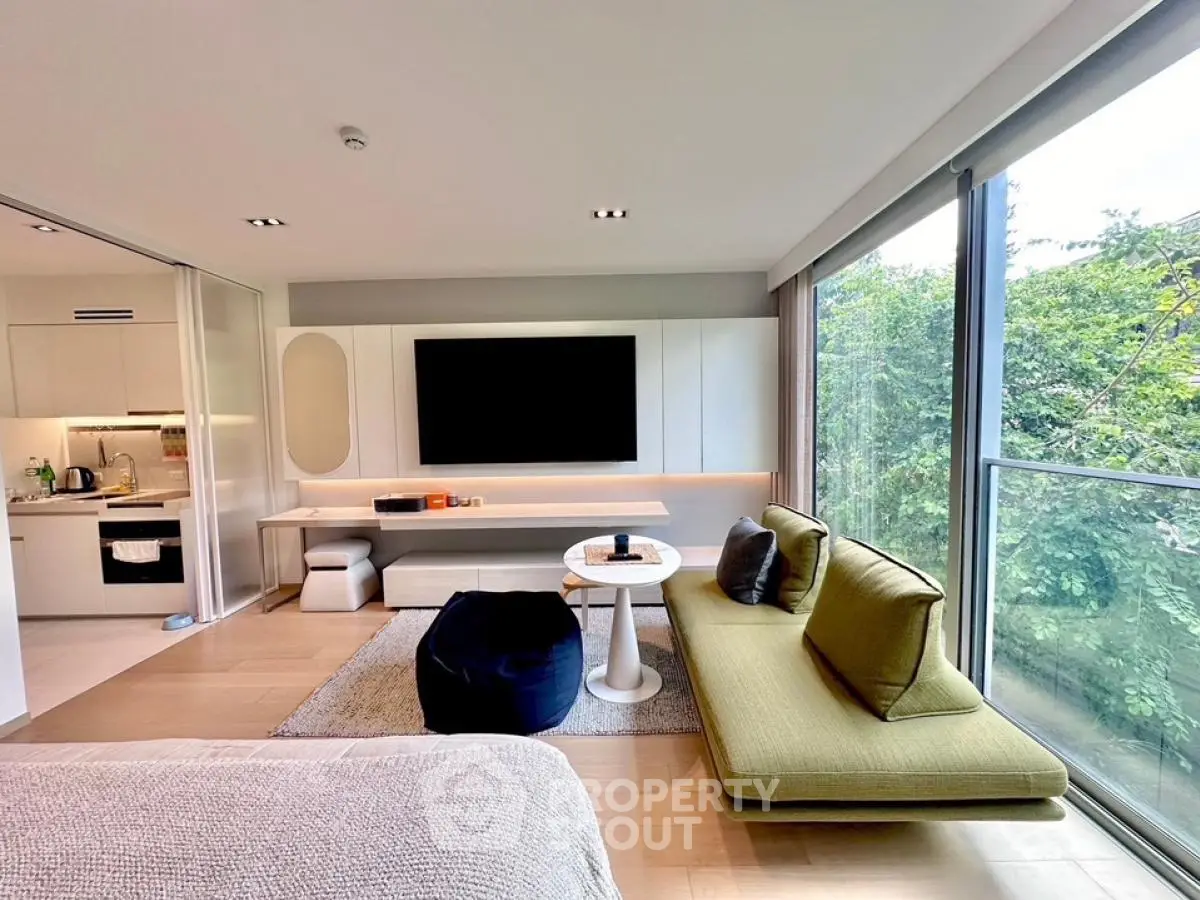Modern living room with large windows and stylish furniture, offering a serene view of greenery.