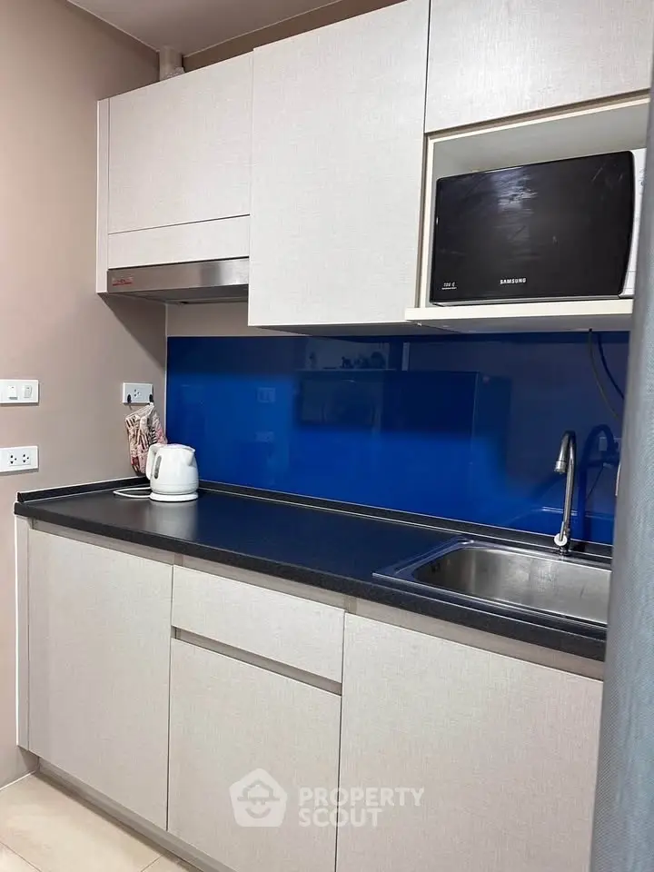 Modern kitchen with sleek cabinetry and blue backsplash, featuring a microwave and kettle.