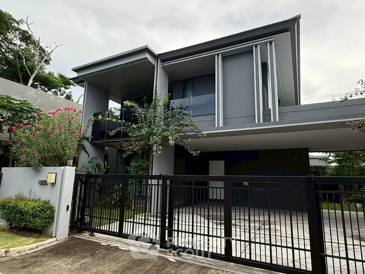 Modern two-story house with sleek design and gated driveway in a lush green setting.