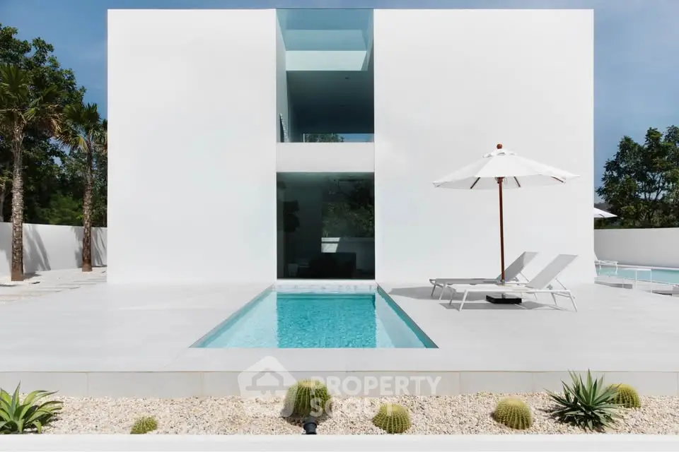 Modern minimalist villa with sleek pool and sun loungers, surrounded by lush greenery.