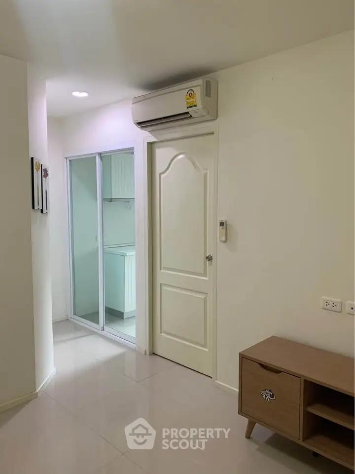 Modern apartment interior with air conditioning and sleek white door leading to kitchen area.