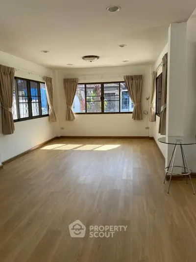Spacious sunlit living room with wooden flooring and large windows in a modern home.