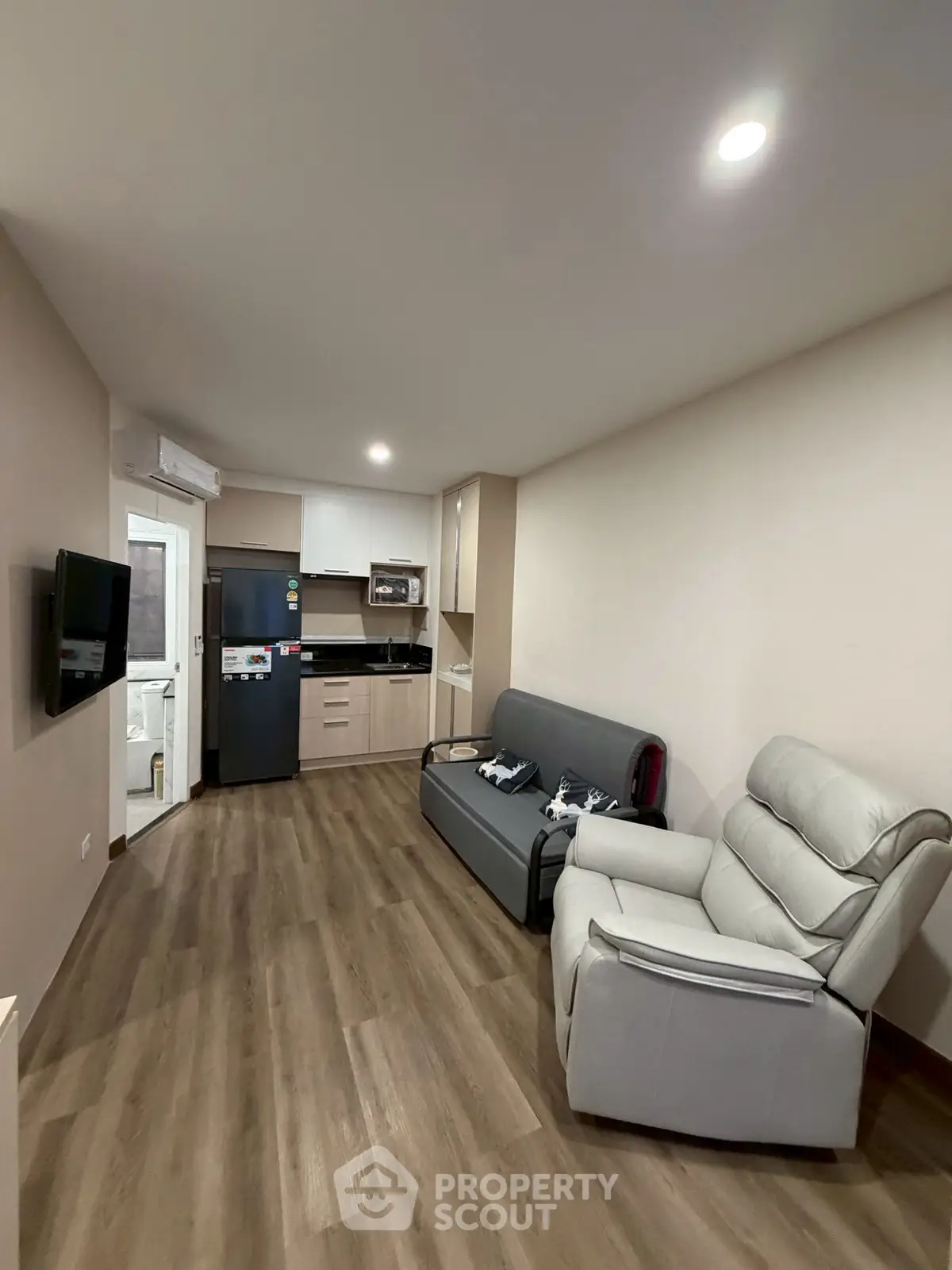 Modern living room with sleek kitchen, cozy seating, and stylish flooring in a compact apartment.
