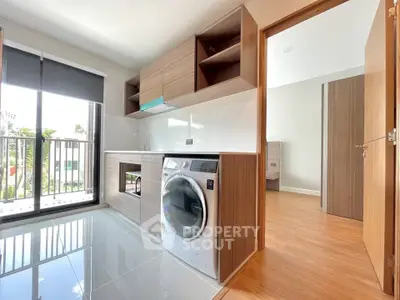 Modern kitchen with sleek cabinetry and built-in washing machine, featuring large windows for natural light.