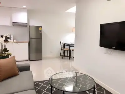 Modern living room with sleek kitchen and dining area, featuring a cozy sofa and wall-mounted TV.
