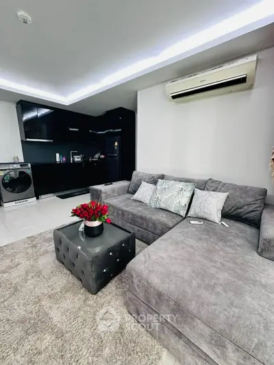Modern living room with plush gray sofa, stylish ottoman, and sleek kitchen in open layout.