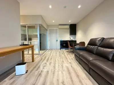 Modern living room with sleek furniture and open layout, featuring wood flooring and glass partition.
