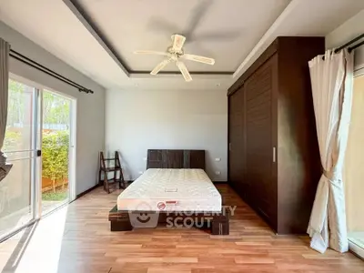 Spacious bedroom with wooden flooring, large window, and ceiling fan in modern home.