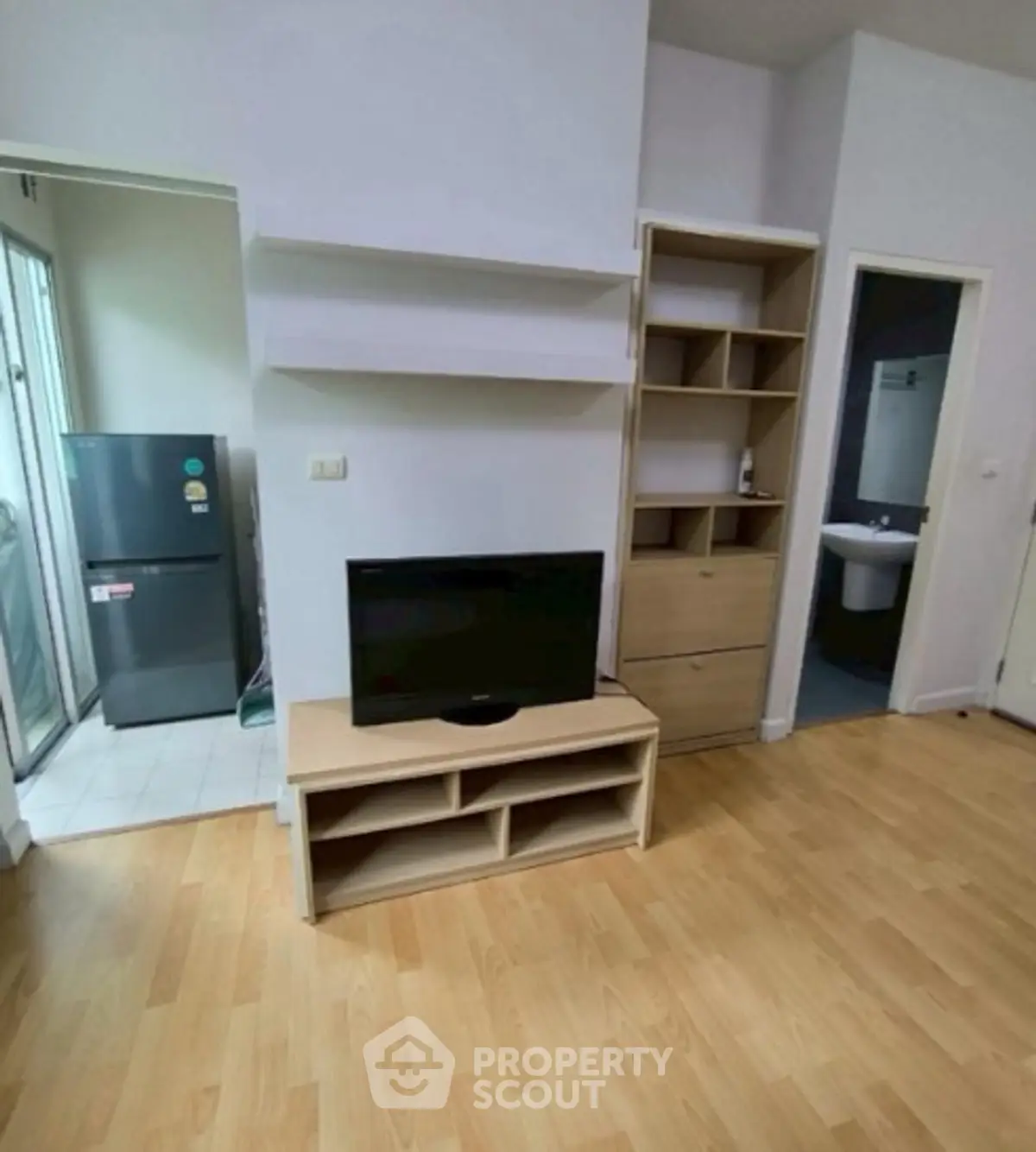 Cozy living room with wooden flooring, TV stand, and open kitchen view in modern apartment.