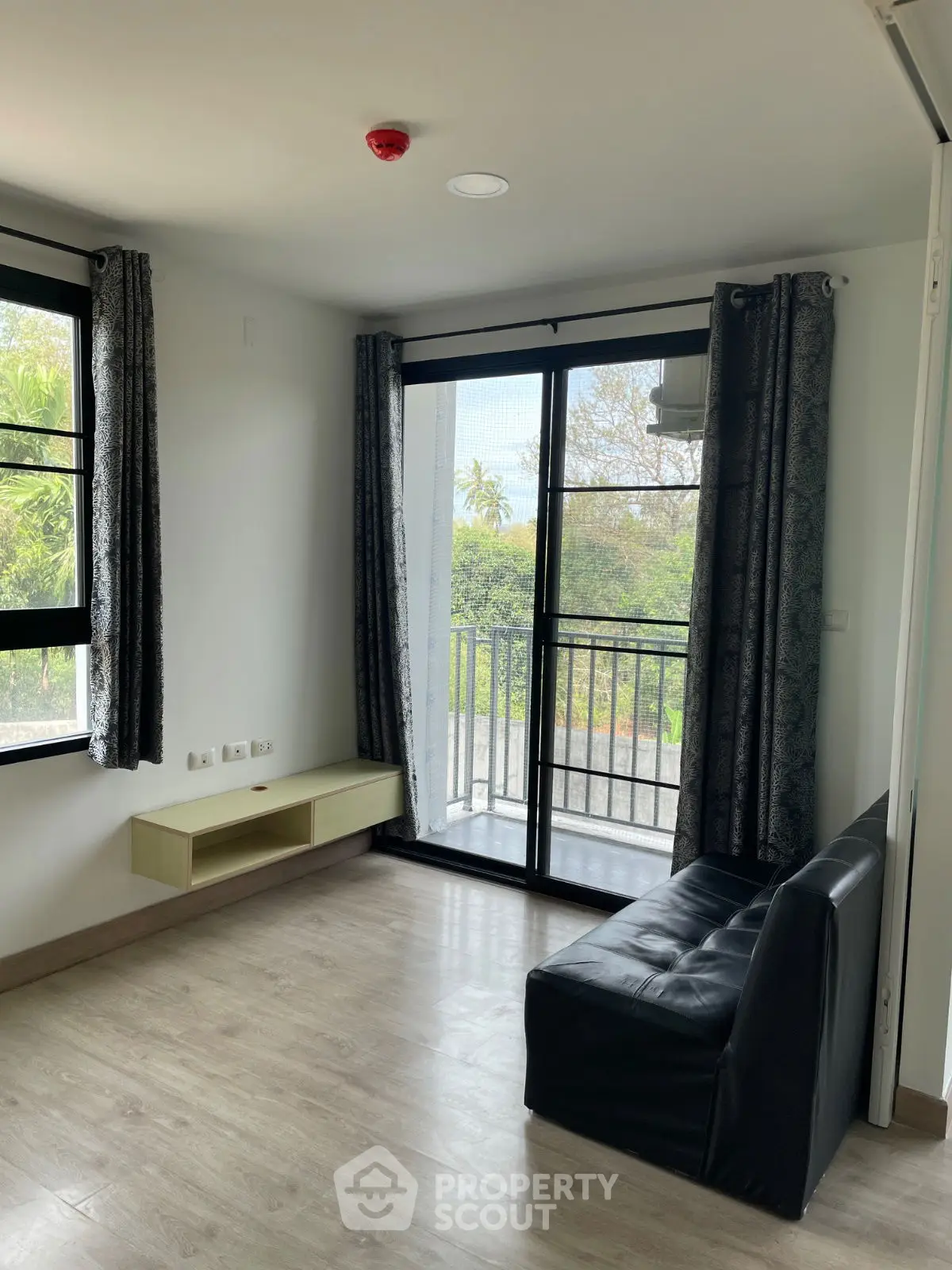 Bright living room with large windows and balcony access, featuring modern flooring and minimalist design.