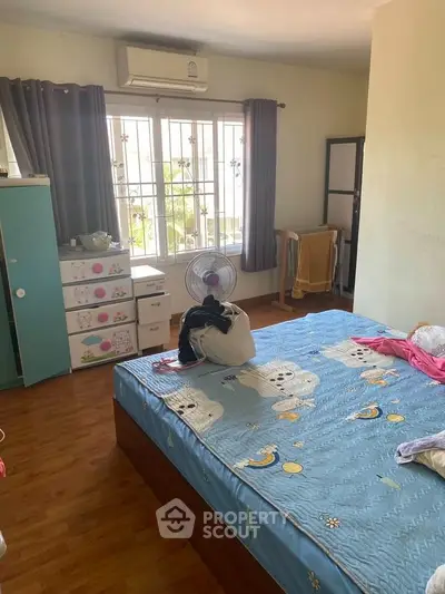 Cozy bedroom with large window, air conditioning, and wooden flooring, perfect for comfortable living.