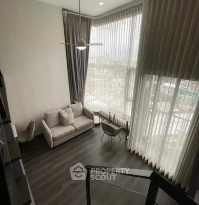 Modern loft-style living room with high ceilings and large windows offering city views.