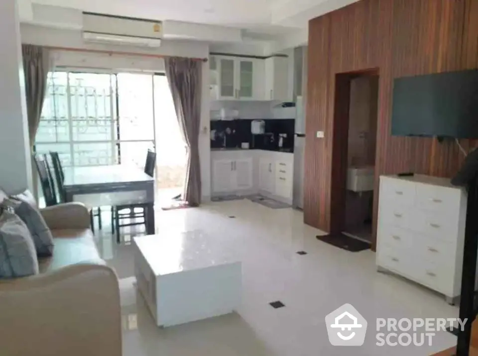 Modern open-layout living room with kitchen and dining area, featuring sleek furniture and ample natural light.