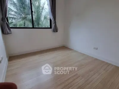 Spacious empty room with wooden flooring and large window overlooking lush greenery.
