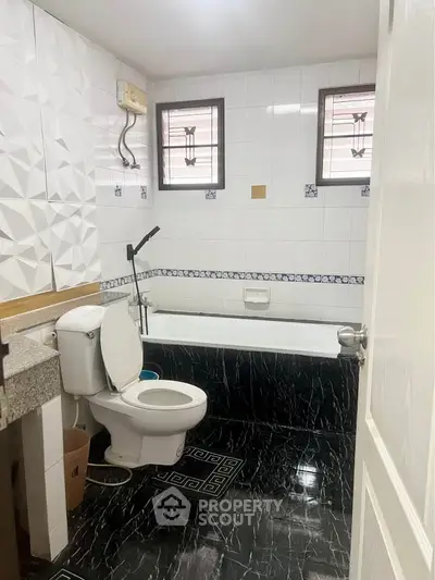 Modern bathroom with stylish black and white tiles, featuring a bathtub and contemporary fixtures.