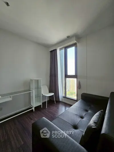 Modern living room with sleek furniture and large window offering city views.