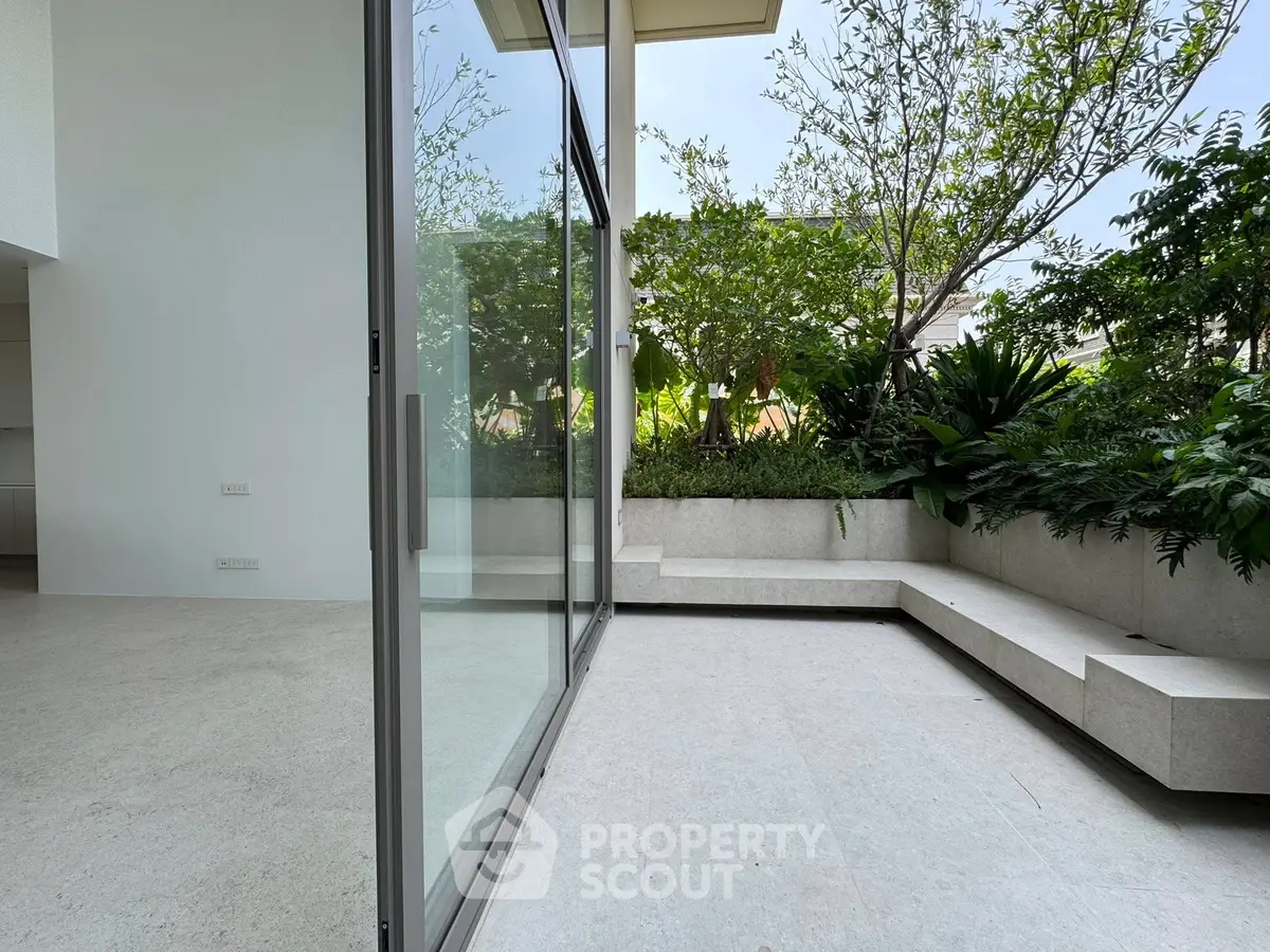 Spacious modern patio with lush greenery and sleek glass doors in a luxury home.