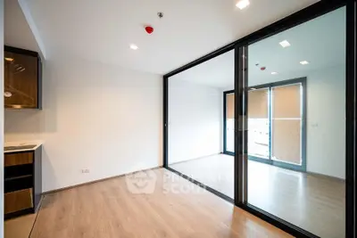Spacious modern living room with large glass doors leading to a balcony, featuring sleek wooden flooring.