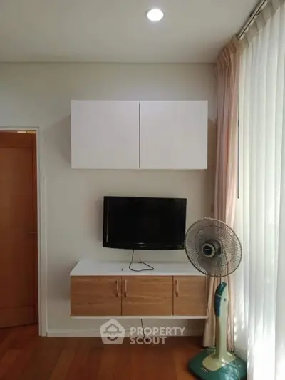 Modern living room corner with TV and fan, wooden flooring, and natural light.