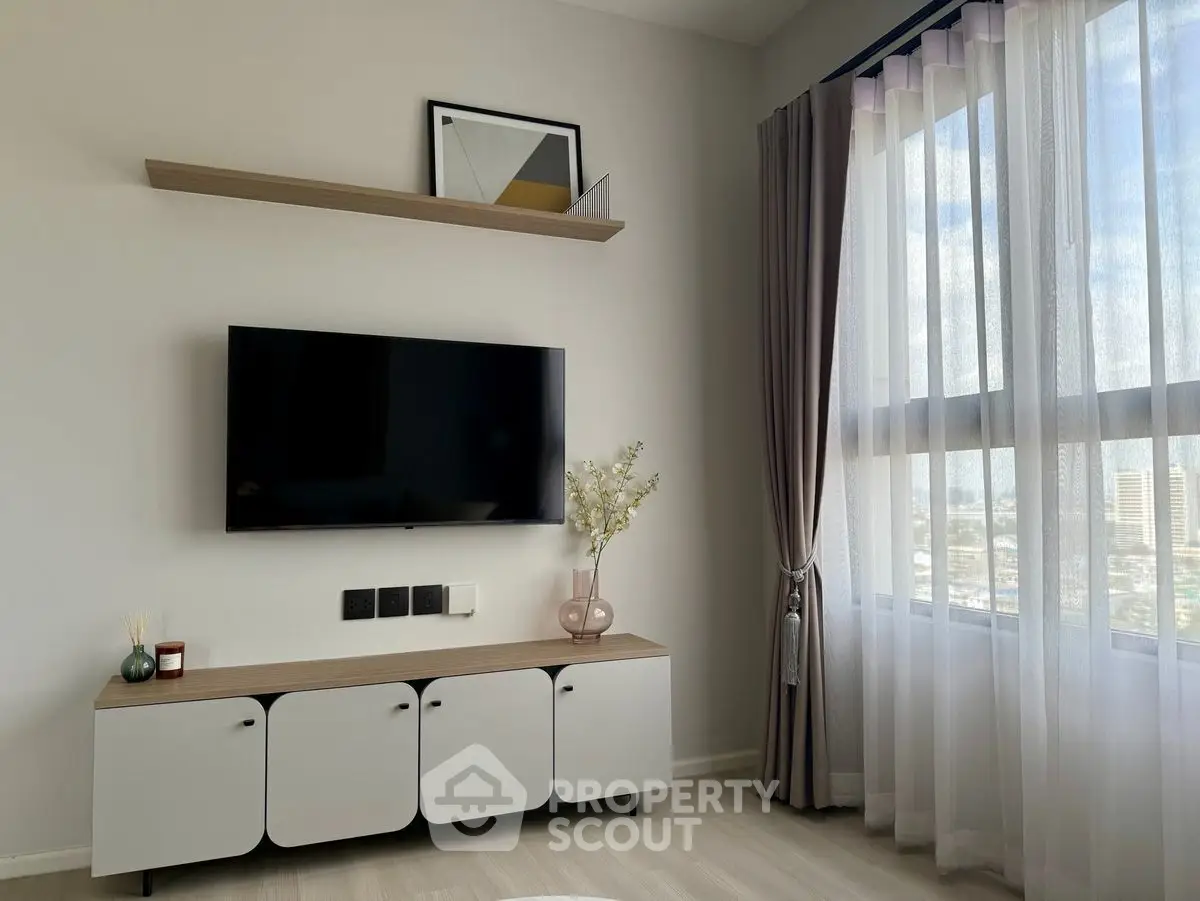 Modern living room with wall-mounted TV, stylish cabinet, and large window with city view.
