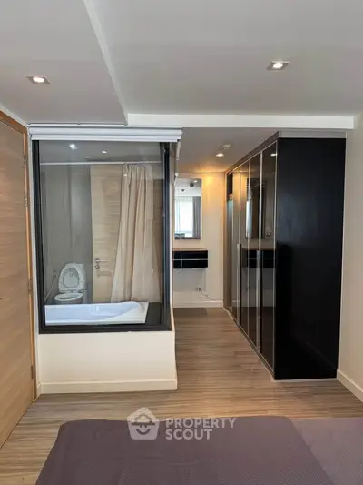 Modern bedroom with glass-enclosed bathtub and sleek wardrobe design