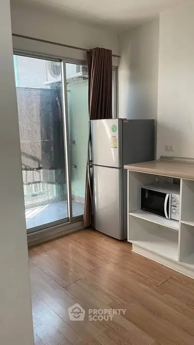Compact kitchen with fridge and microwave, wooden flooring, and balcony access in modern apartment.