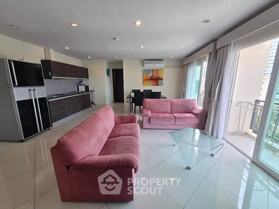 Spacious modern living room with pink sofas, glass table, and balcony view in a high-rise apartment.