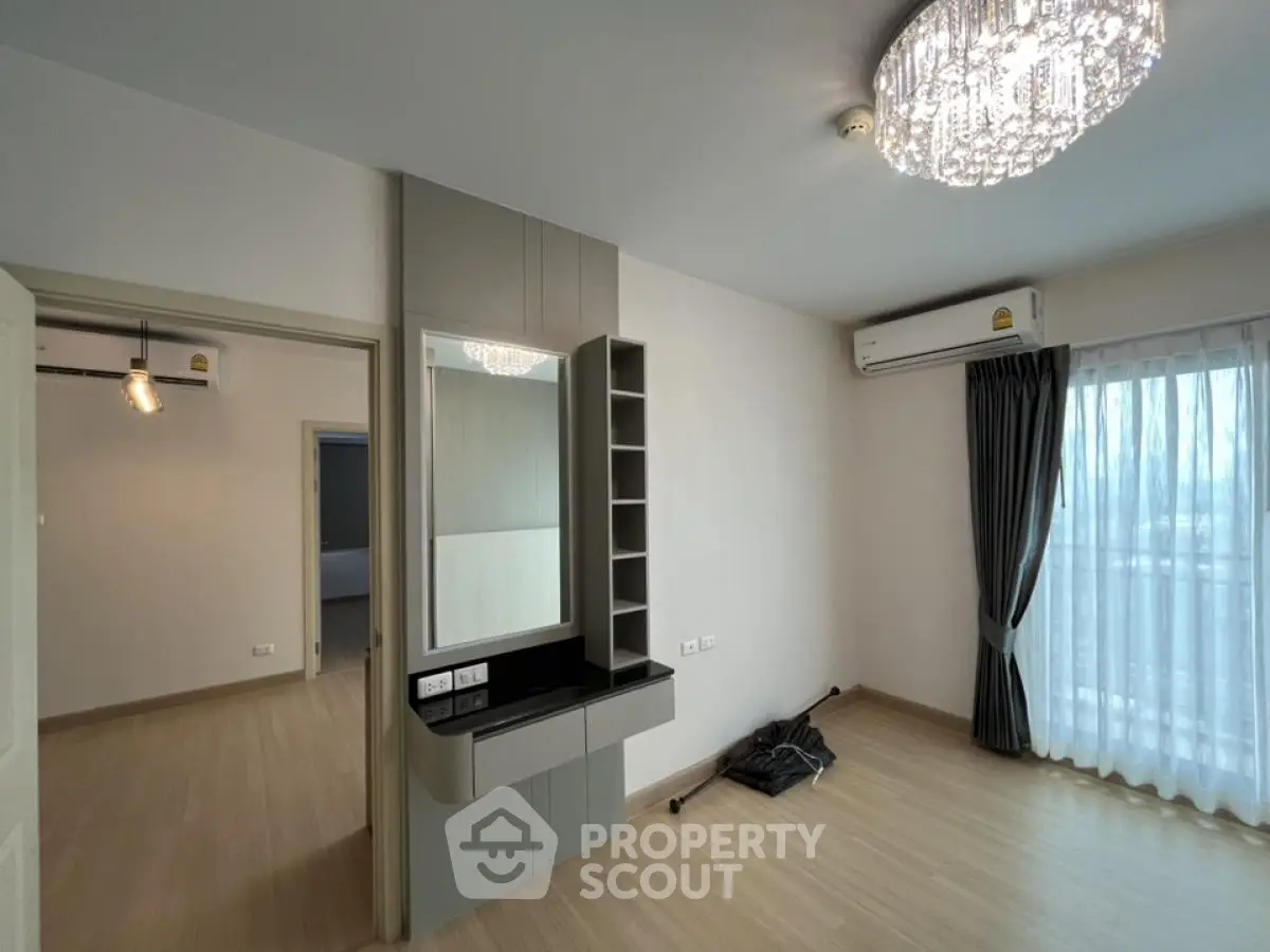 Modern bedroom with elegant chandelier and large window, featuring built-in vanity and air conditioning.