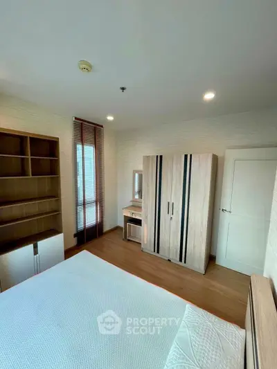 Spacious bedroom with modern wooden furniture and ample natural light.
