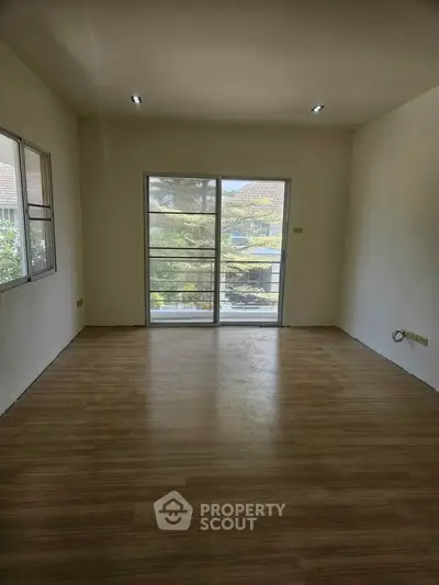 Spacious empty room with large window and wooden flooring, perfect for customization.