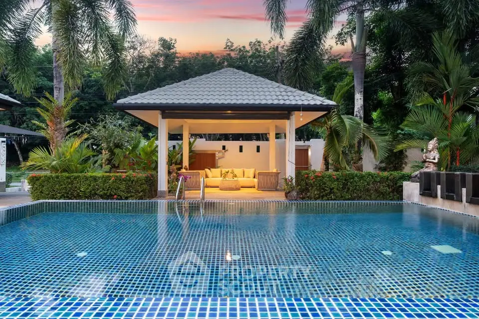 Luxurious tropical villa with stunning pool and lush garden at sunset, perfect for relaxation and entertainment.