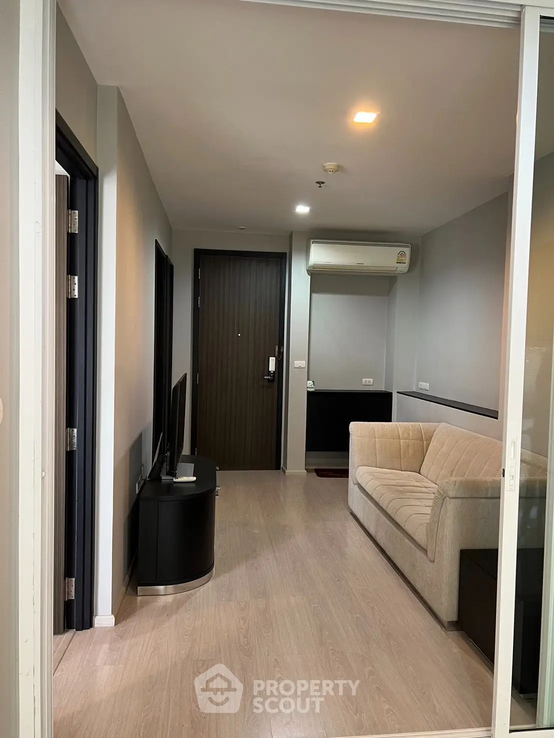 Modern living room with sleek design and cozy beige sofa, featuring a flat-screen TV and wooden flooring.