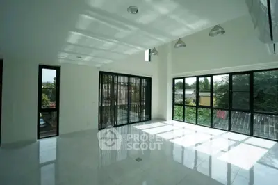 Spacious sunlit living room with large windows and modern lighting