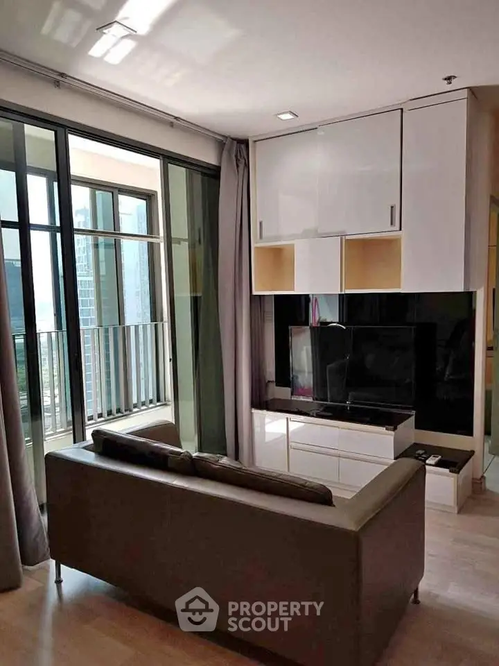 Modern living room with sleek furniture and large windows leading to a balcony with city views.