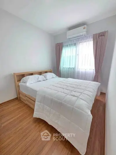 Cozy bedroom with wooden flooring and natural light through large window.