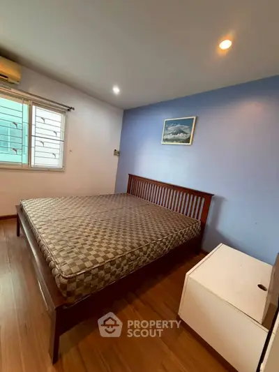 Spacious bedroom with wooden flooring and large window for natural light.